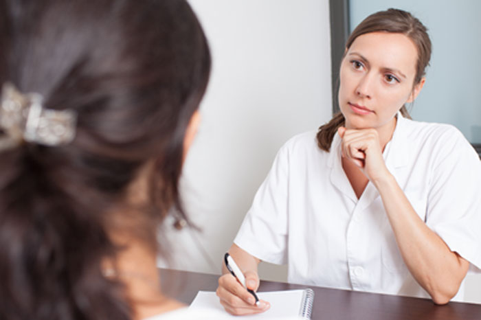 Die Sicherheit, Vorstufen von Gebärmutterhalskrebs bei der Vorsorge zu erkennen, ist abhängig von Abstrichmethode. Neben dem konventionellen Pap-Test und der Dünnschichtzytologie gibt es jetzt auch den S-Pap Test mit höchster Sicherheit.
Ärztin in weißem Kittel am Schreibtisch sitzend mit Kugelschreiber und Schreibblock berät konzentriert eine Patientin, die ihr gegenüber sitzt und von der nur nur braune Haare mit Haarspange im linken Bildrand vonhinten zu sehen sind.